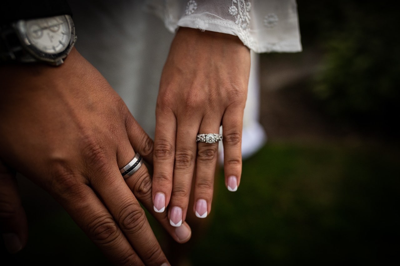 A husband and wife touching hands and able to see their bridal rings