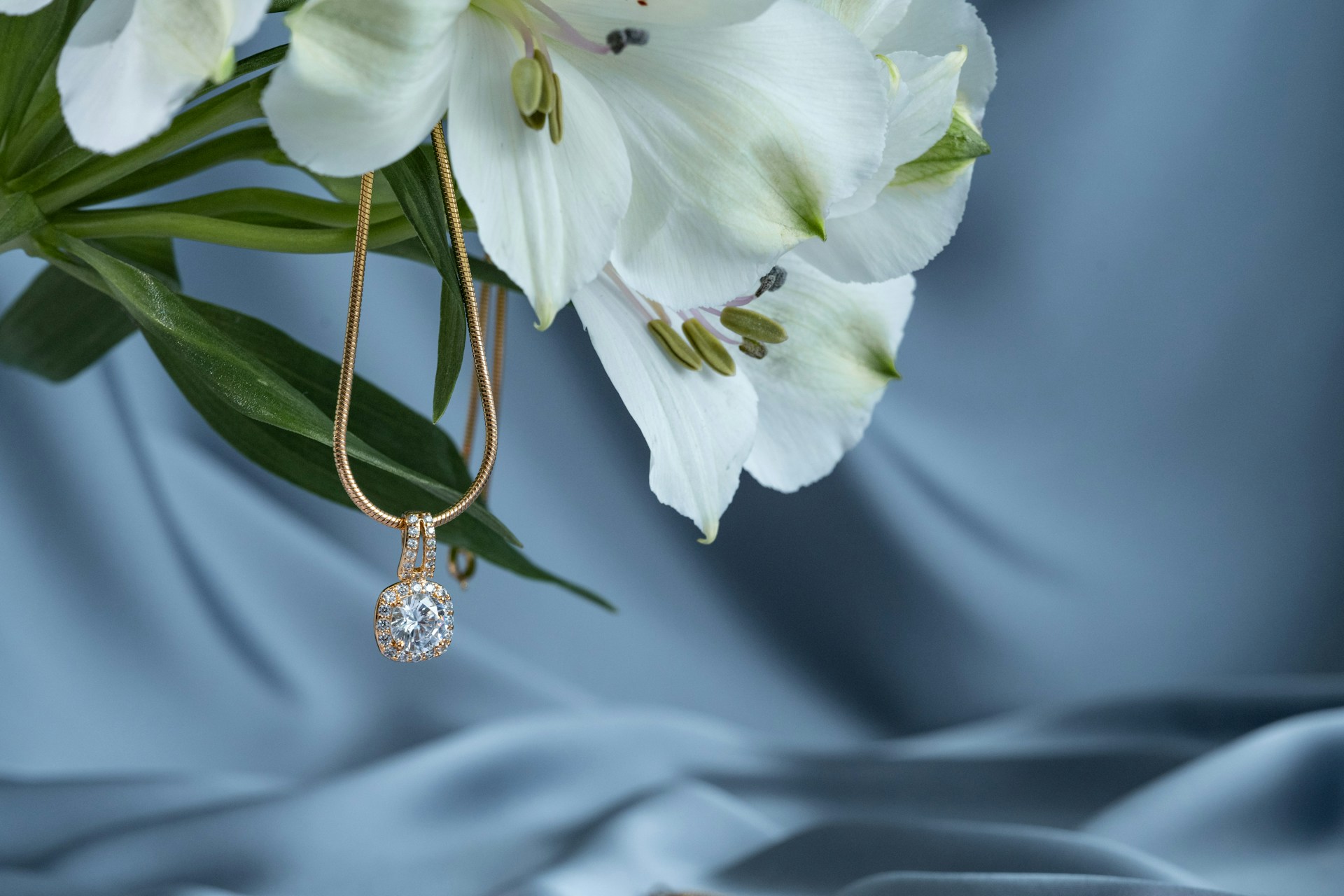 a yellow gold diamond pendant necklace hanging from a bouquet of white flowers