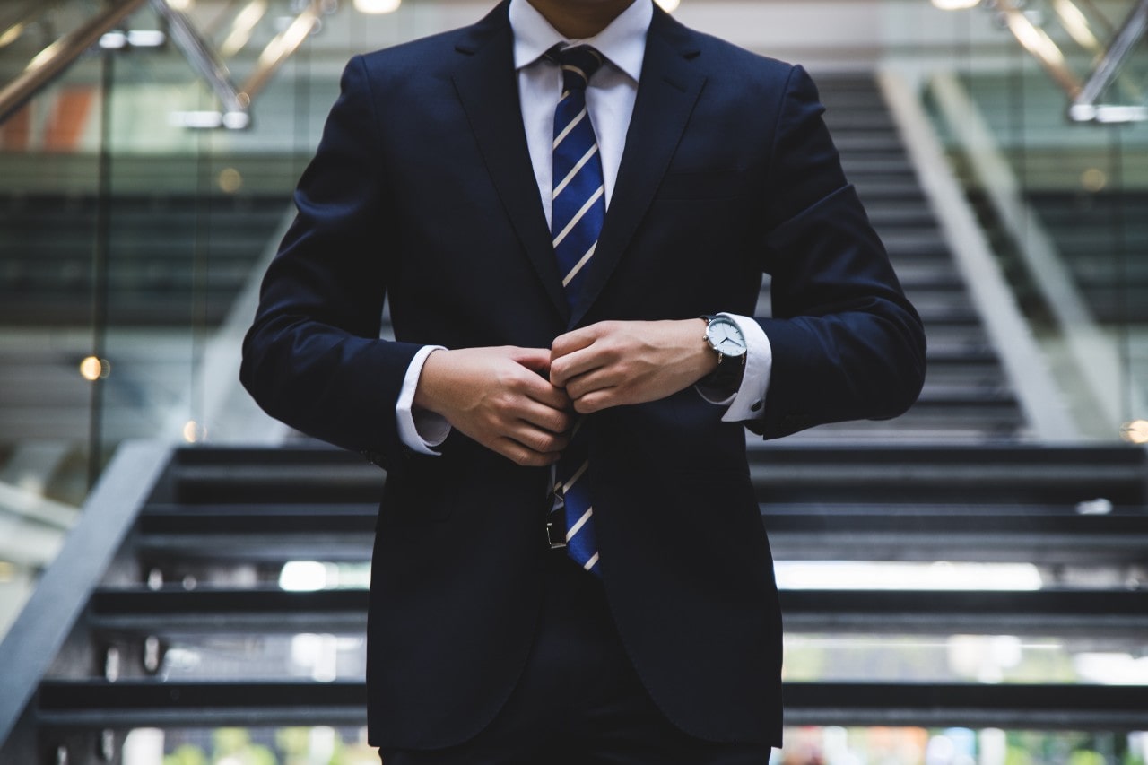 a man in a suit wearing a dress watch by a staircase