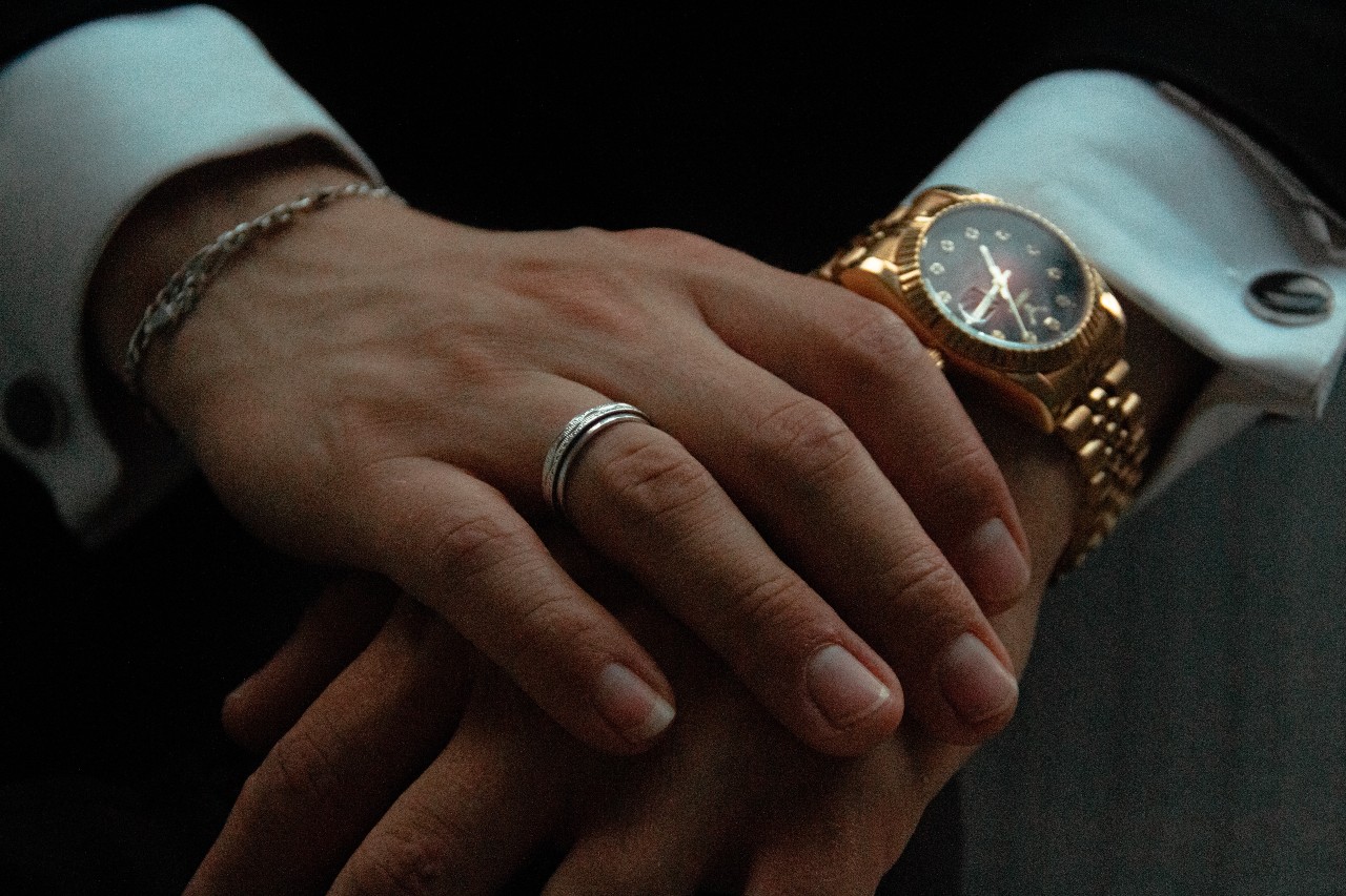 A close-up of a well-dressed man’s hands, adorned in an elegant dress watch and simple fashion jewelry.