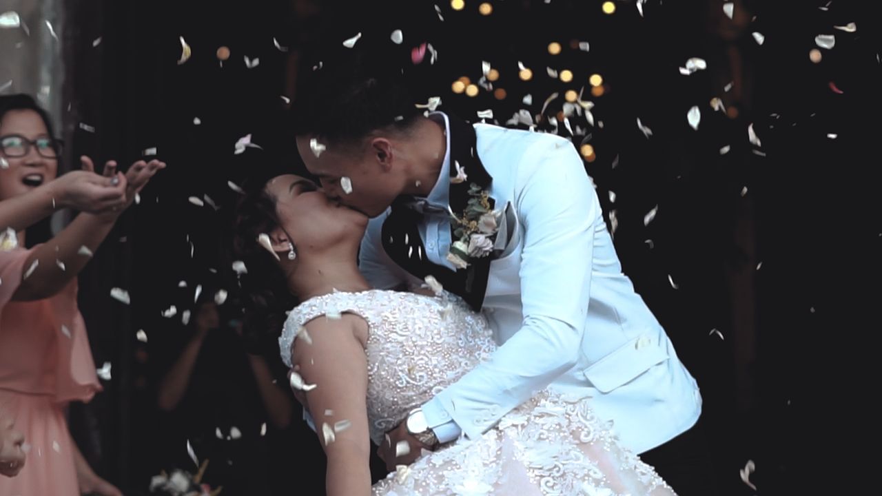 A romantic exit to church wedding with guests throwing white rose petals and the married couple is sharing a kiss