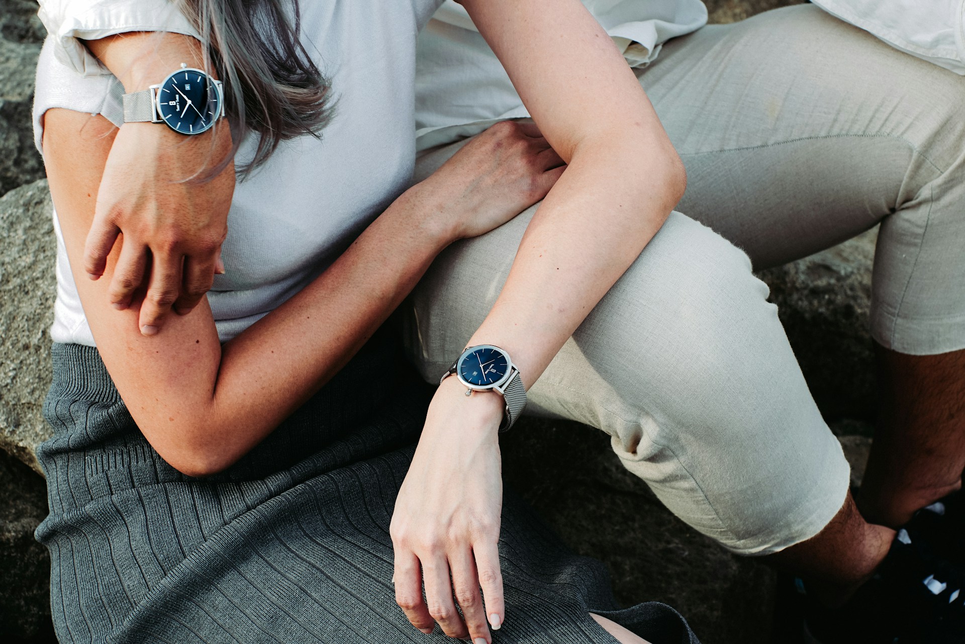 A couple sitting together and wearing matching blue and silver watches.