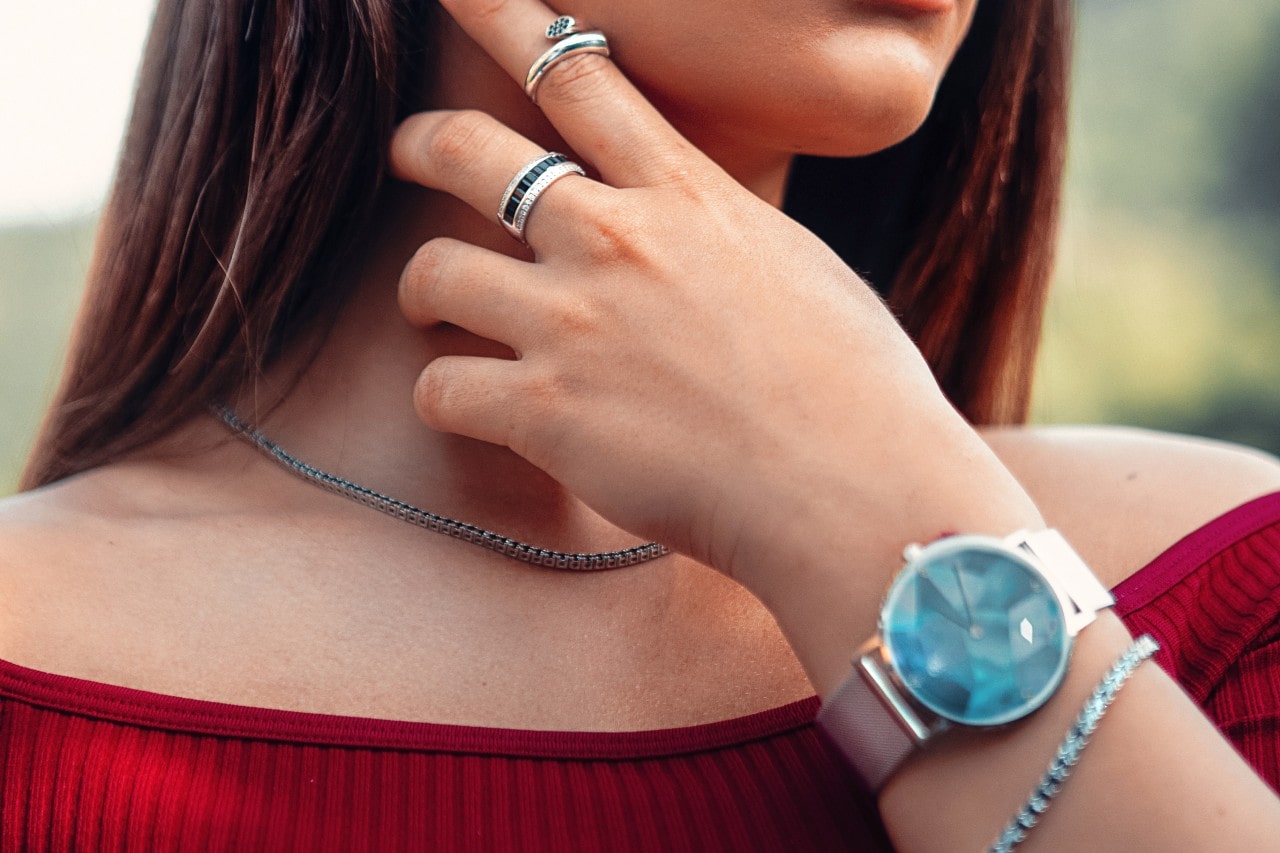 a lady’s hand and neck wearing a luxury watch and jewelry