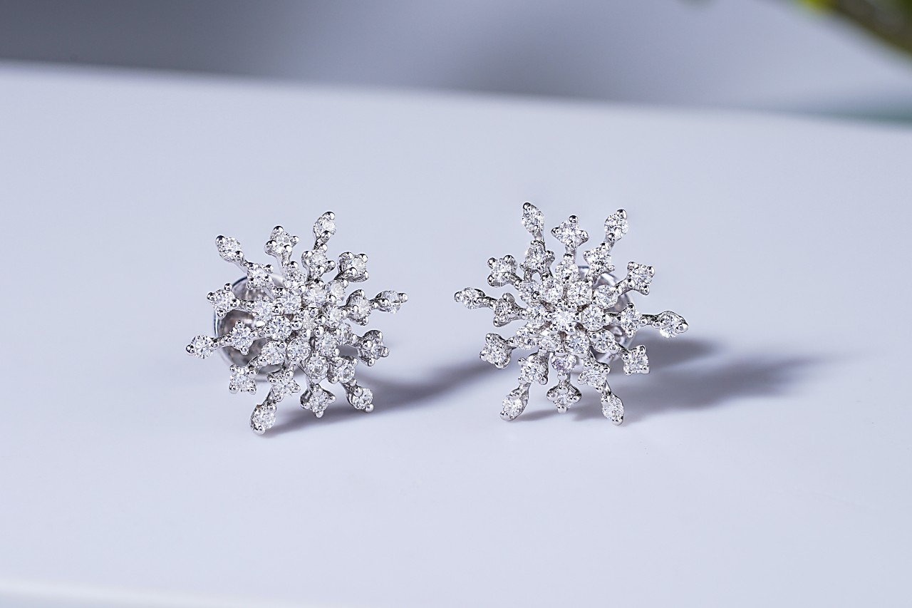 A pair of snowflake shaped diamond stud earrings on a white surface.