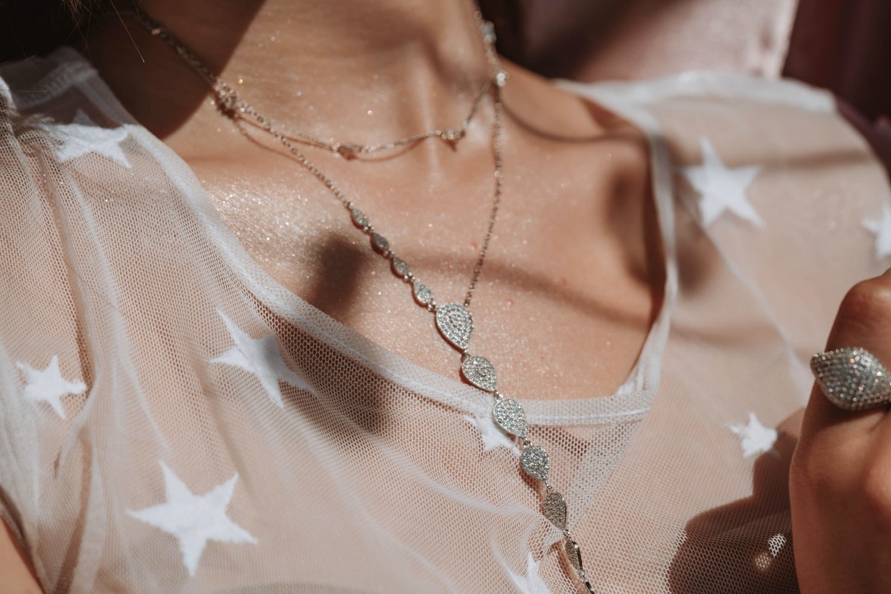 A close up image of a woman’s neckline adorned with a layered diamond necklace.