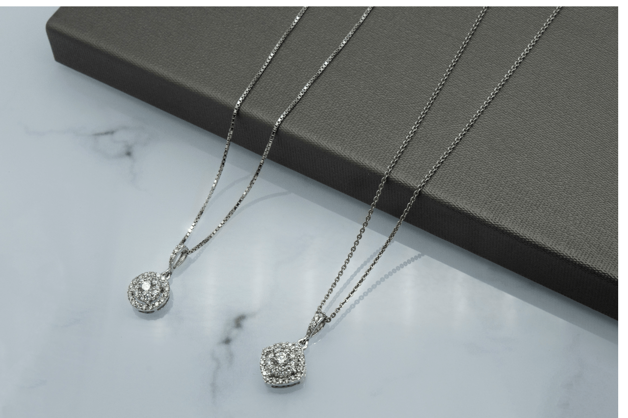 Two white gold diamond pendant necklaces lying side by side.