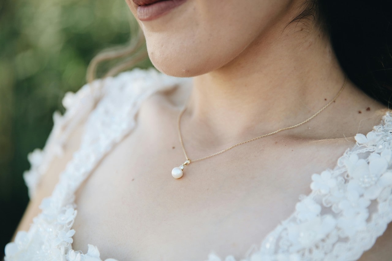 A close-up image of a bride’s neckline adorned with a simple pearl pendant necklace.