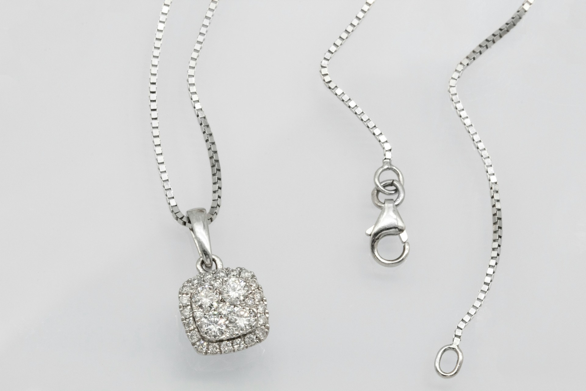 A close-up of a white gold necklace with a square diamond halo pendant.