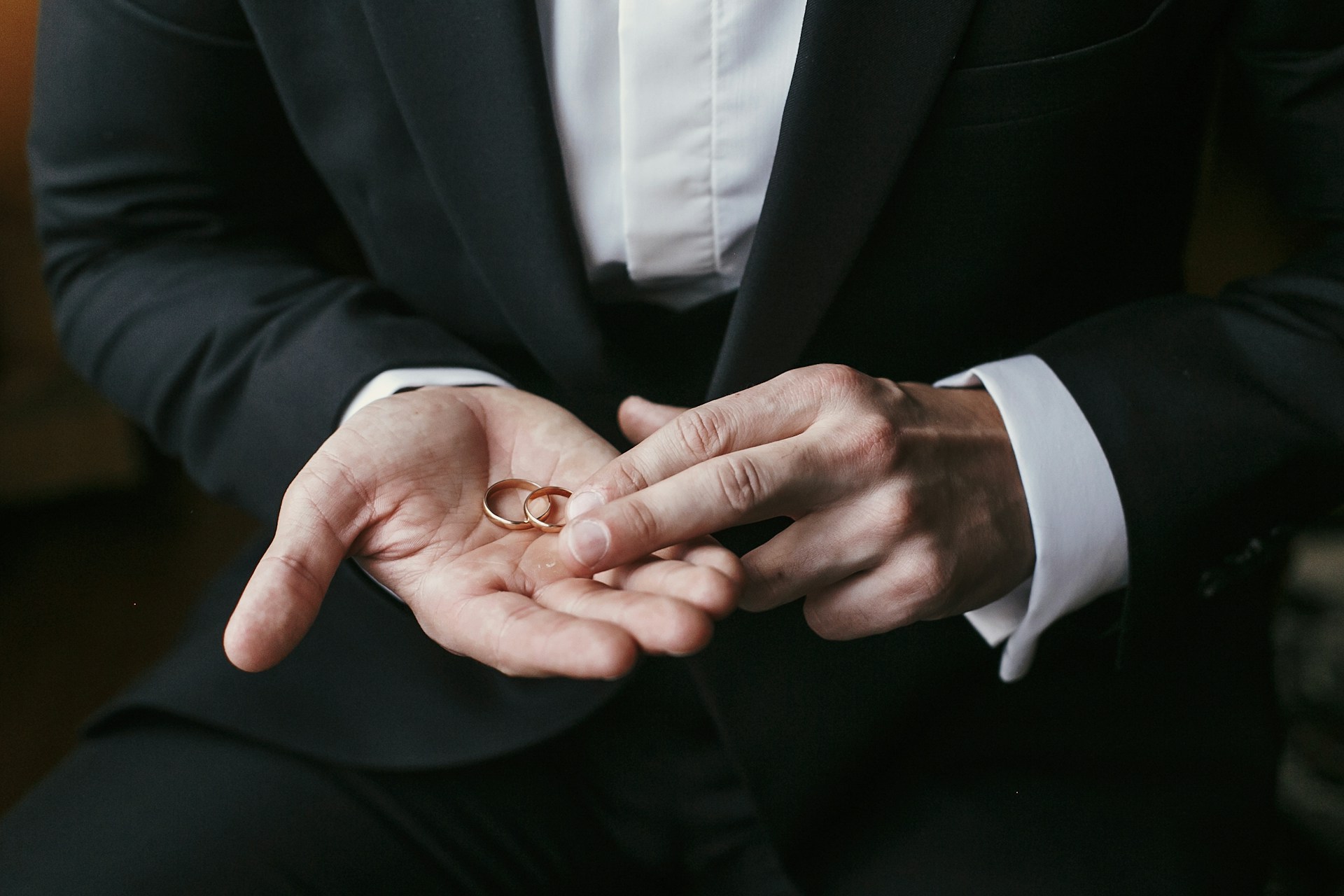 a groom holding two yellow gold wedding bands in the palm of his hand