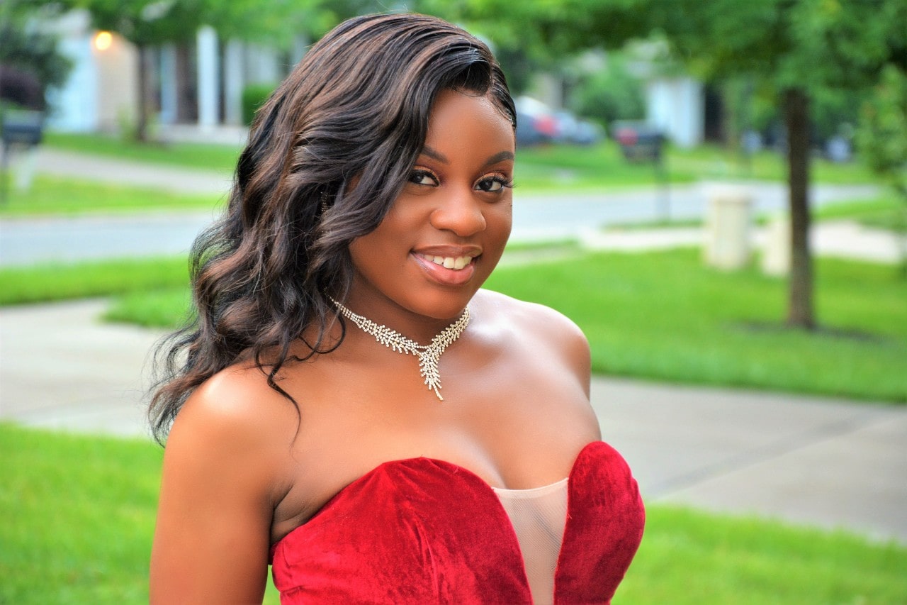 A close-up of a young woman in a velvet dress, wearing a distinct diamond necklace.