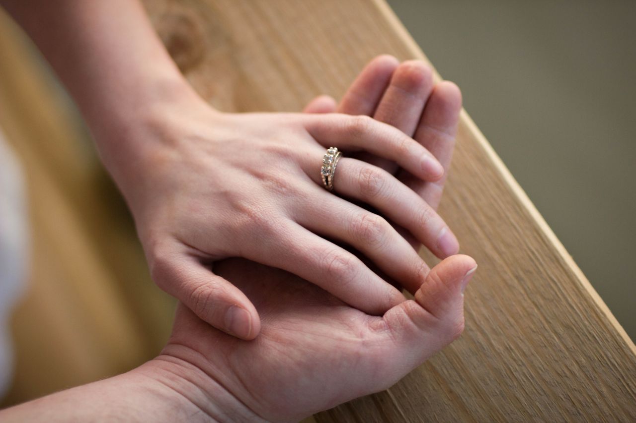 A closeup of a couple’s hands on a wooden bench.