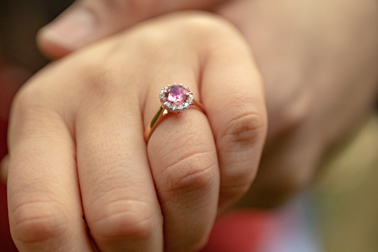 close up image of a person’s had wearing a rose gold ring with a halo setting a purple center stone