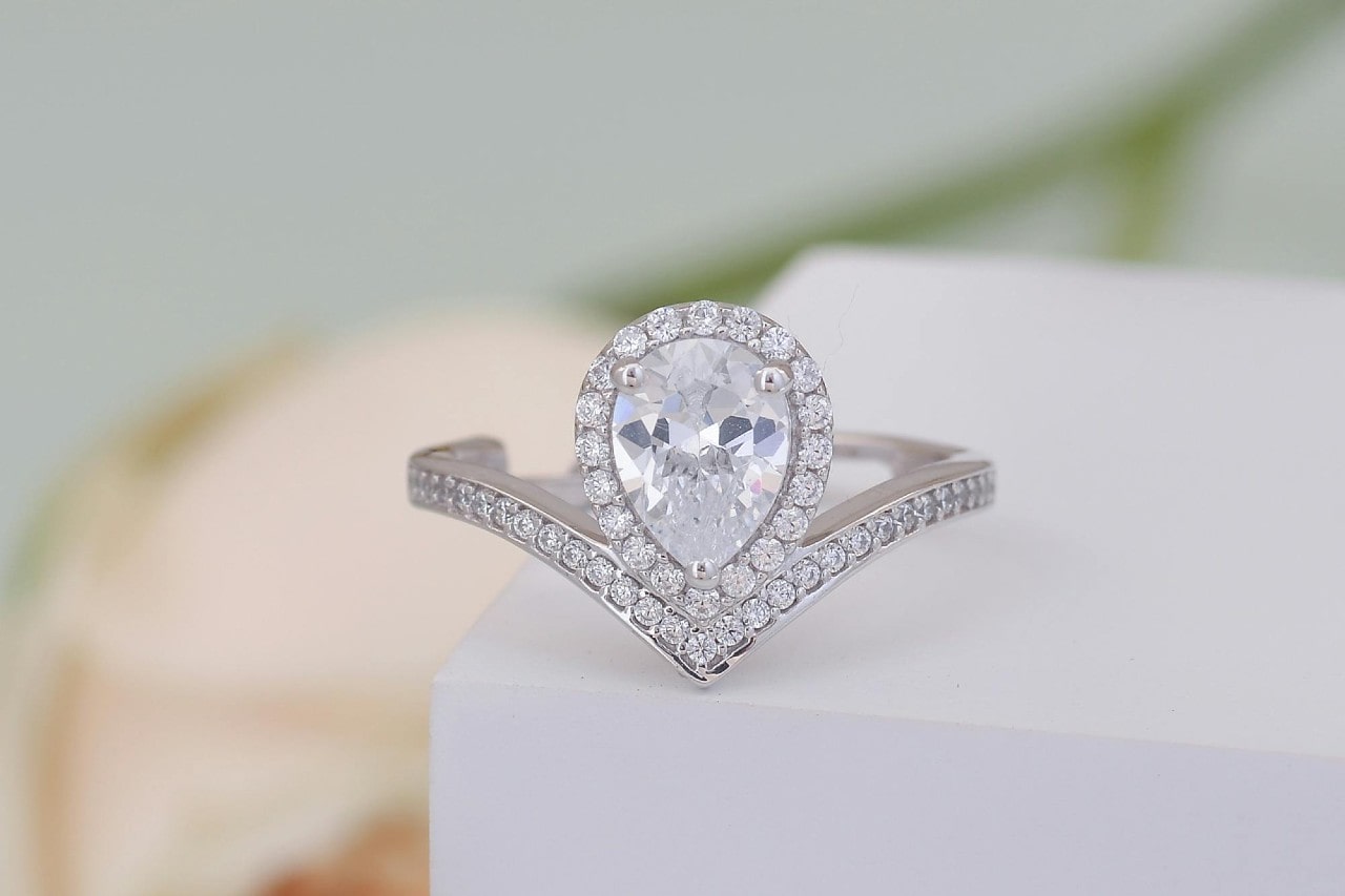 a pear shape engagement ring featuring a curved band and a halo setting
