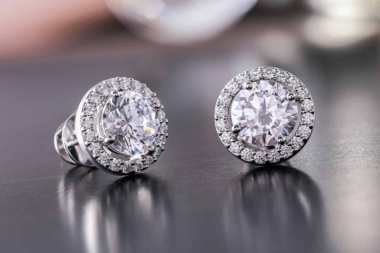 a pair of white gold diamond halo stud earrings on a metallic service.