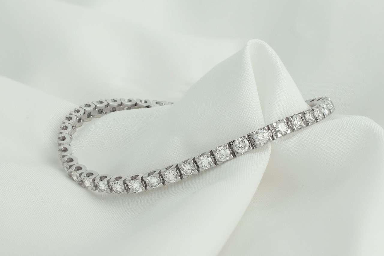 a white gold diamond tennis bracelet sitting on a piece of white fabric.