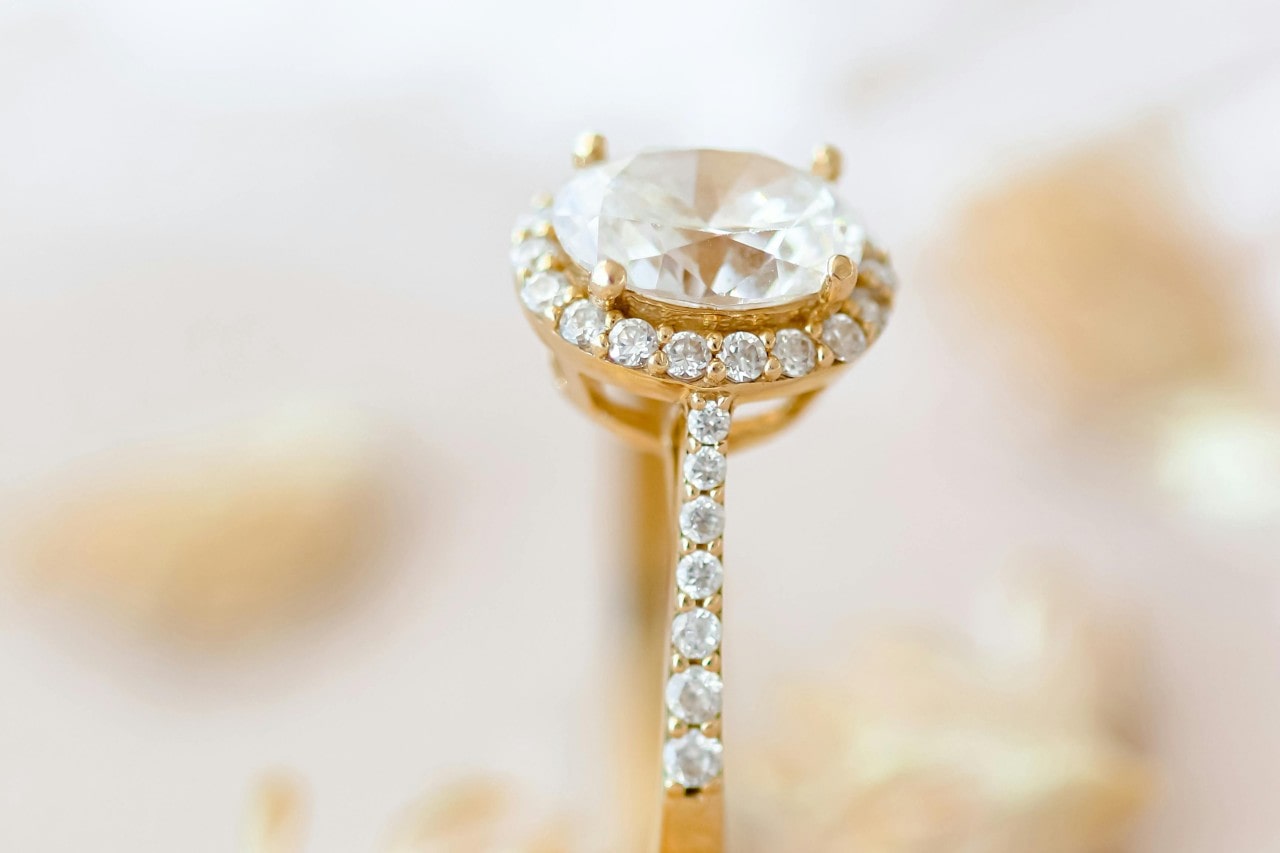 close up image of a yellow gold, oval cut halo engagement ring with side stones