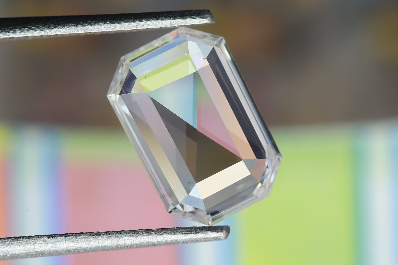 A close-up of a stunning emerald-cut diamond, carefully held by jeweler’s tweezers.