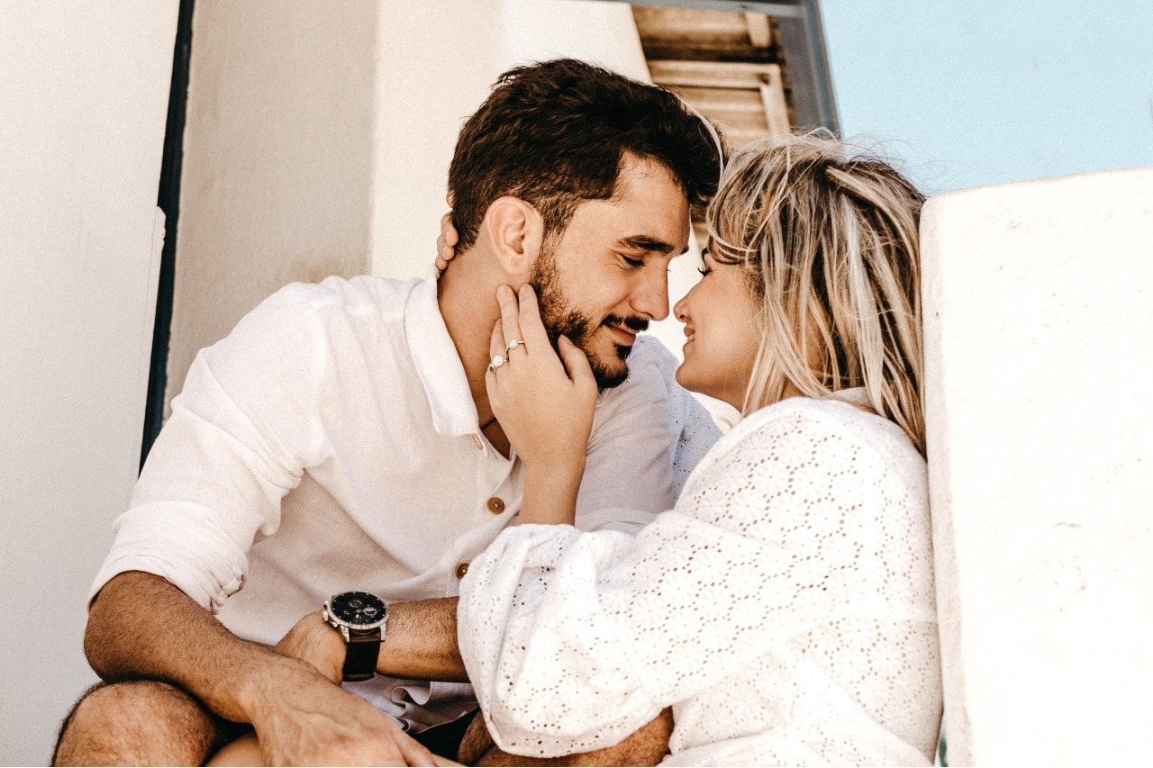 An engaged couple shares an intimate moment sitting on outdoor steps.