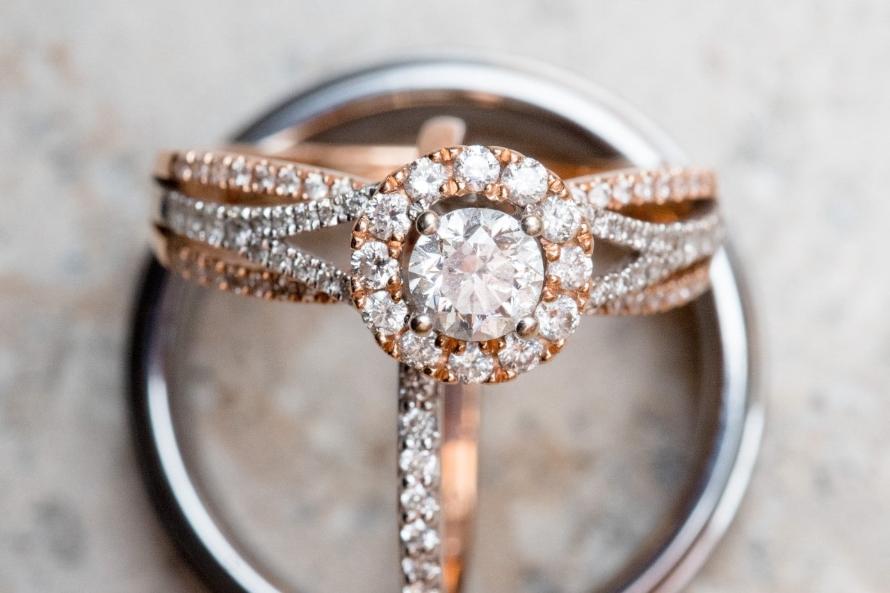 A rose gold and white gold halo engagement ring with two wedding bands.